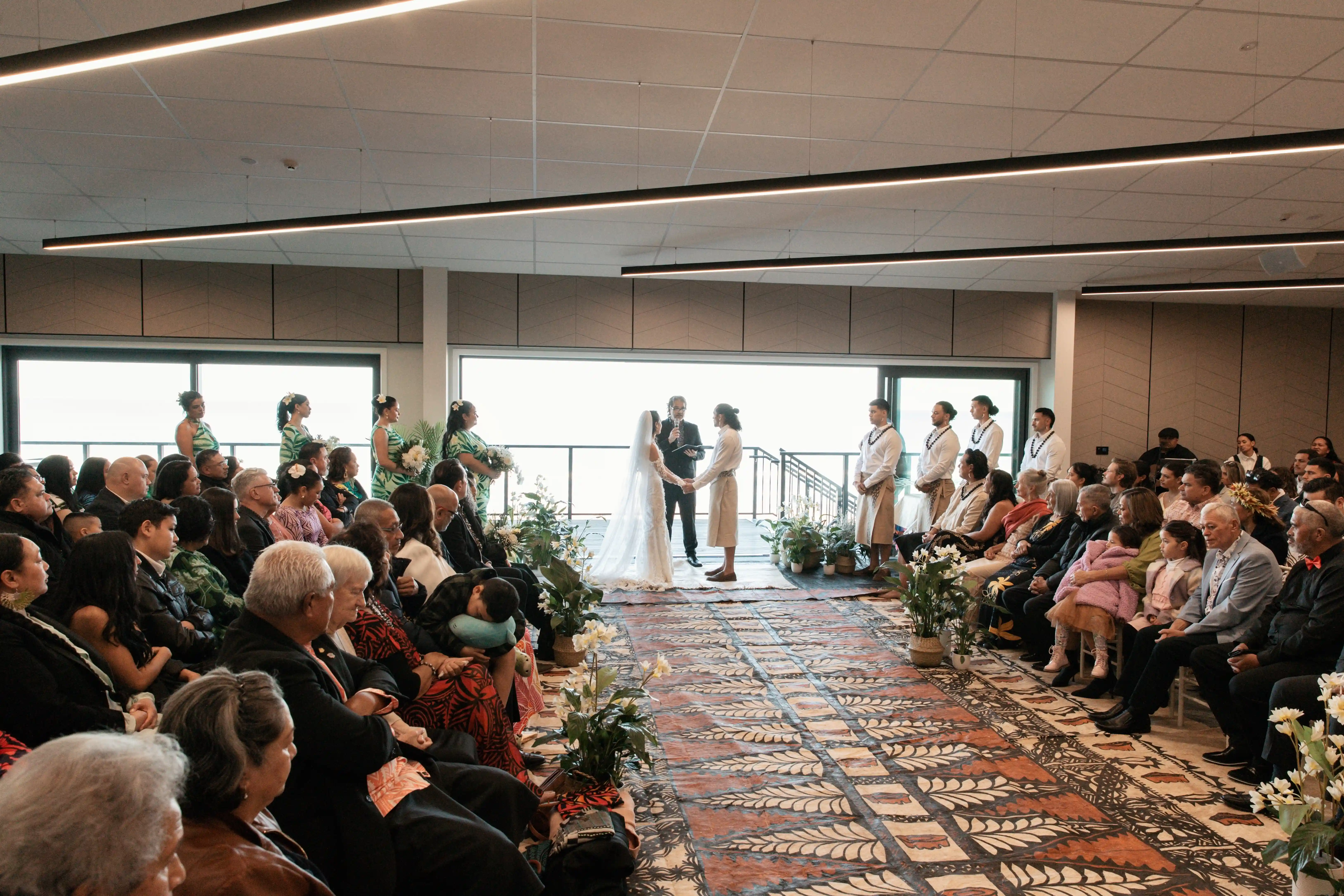 Indoor wedding ceremony at Gisborne beachfront venue with seated guests and ocean view windows