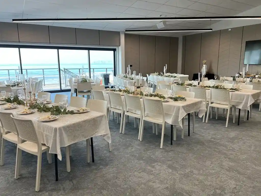 Gisborne beachfront wedding venue with sliding glass doors open to beach deck, reception tables with greenery