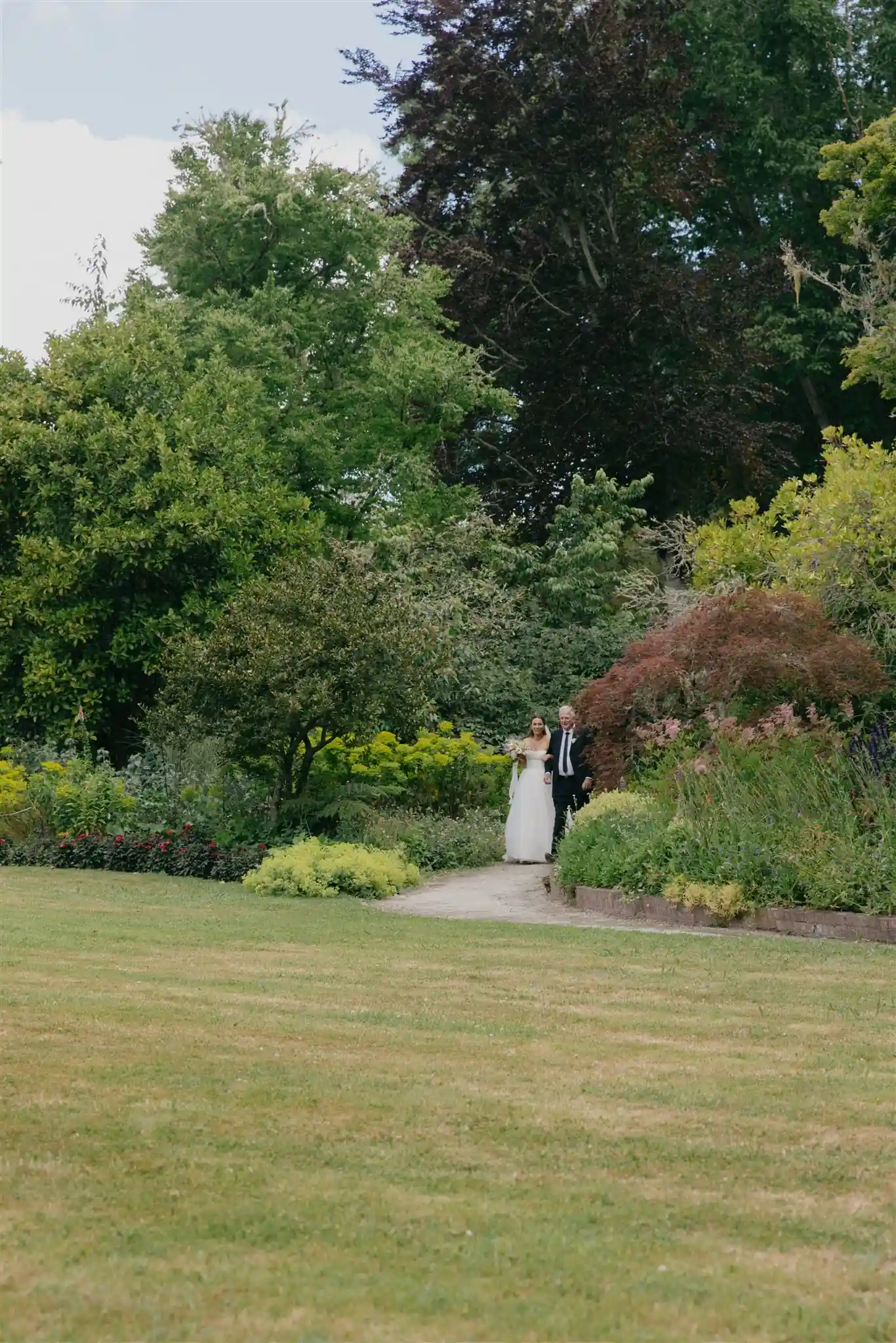 Bride and groom on garden path through lush arboretum grounds