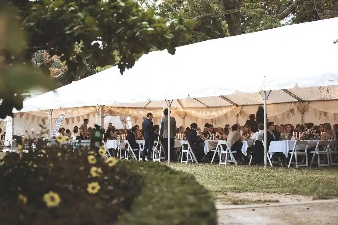 Wedding reception marquee tent with guests seated at long tables with bunting and festoon lights inside